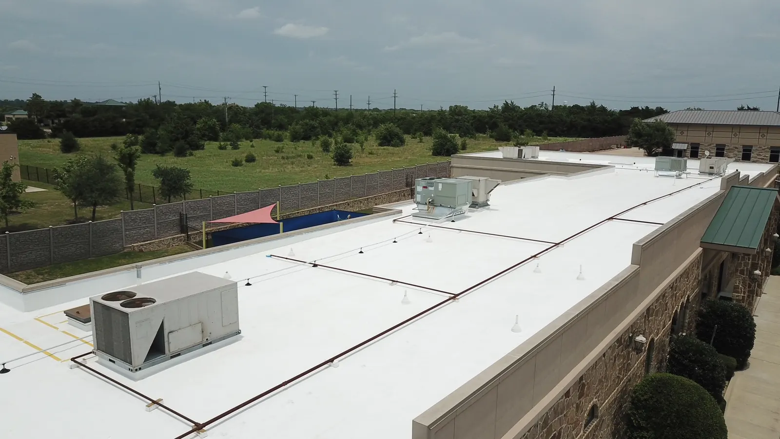 Long run of completed white TPO roof along a stone commercial building parapet